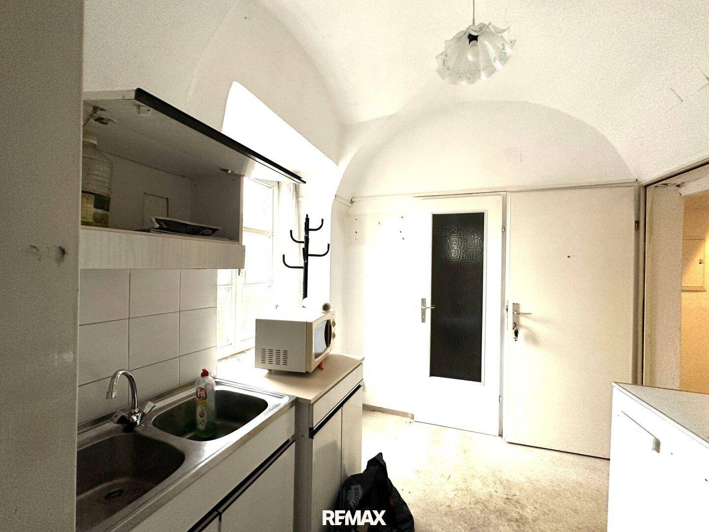 Kleine Küchenzeile mit Spüle, Mikrowelle und Fenster, ideal für eine Singlewohnung.