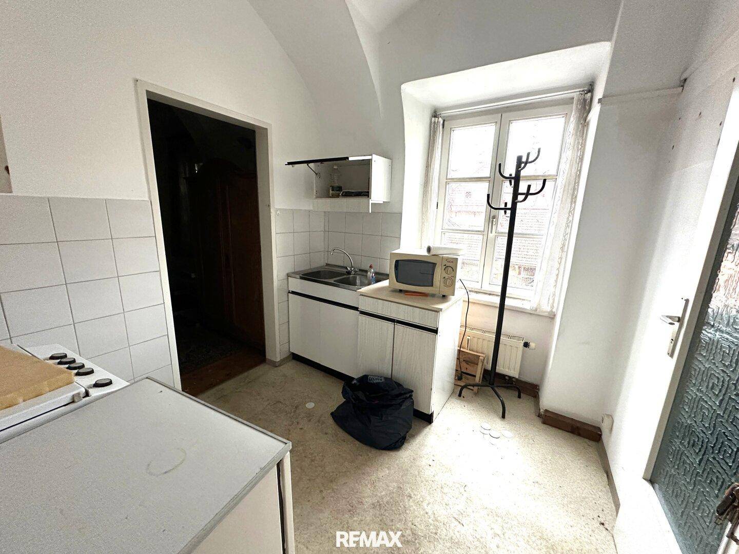 Kompakte Küchenzeile mit Spüle, Mikrowelle und einem Fenster, das Tageslicht spendet.