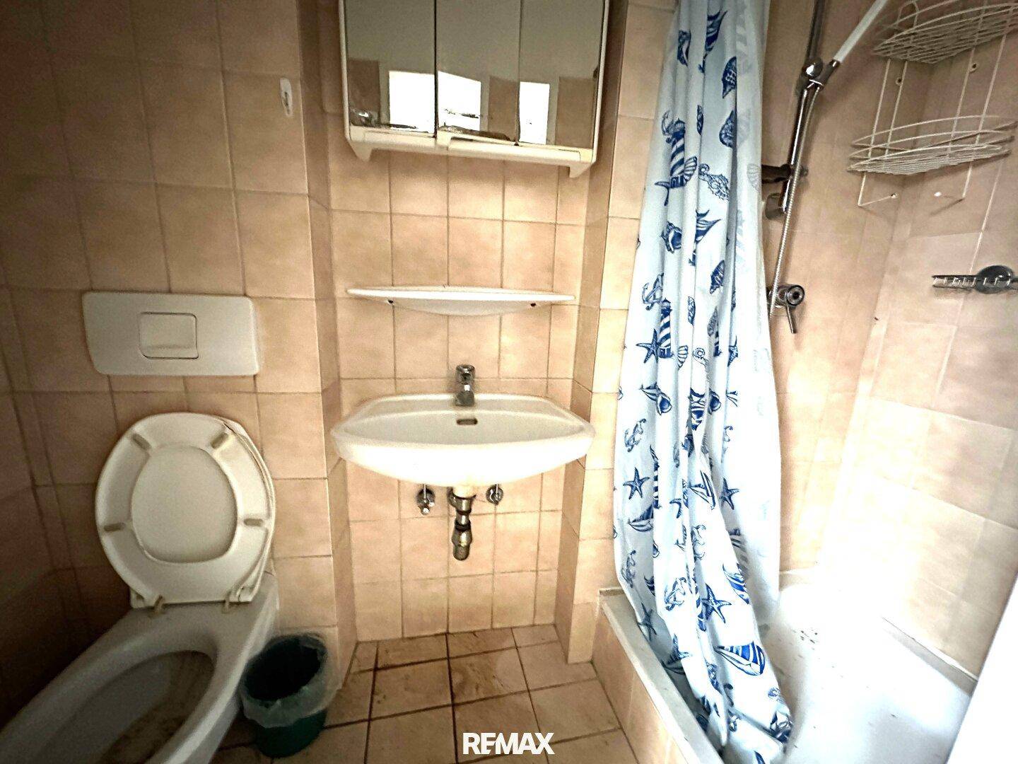 Badezimmer mit Badewanne, Duschvorhang, Waschbecken und Toilette, gefliest in Beige.