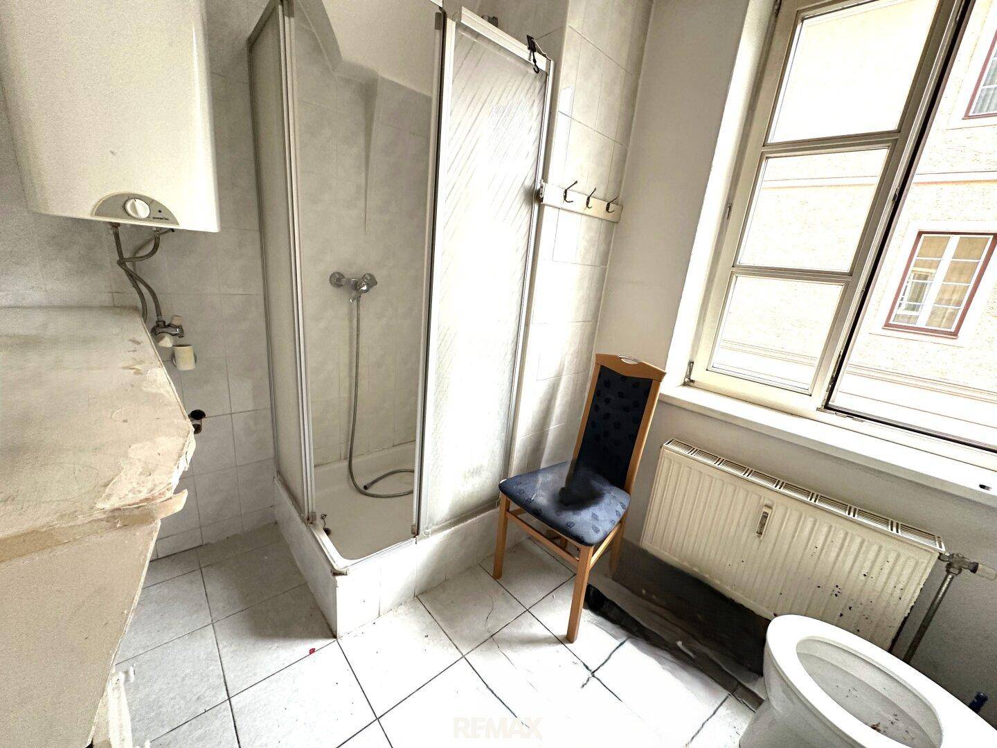 Badezimmer mit Duschkabine, Toilette und Heizkörper, bereit für eine Modernisierung.