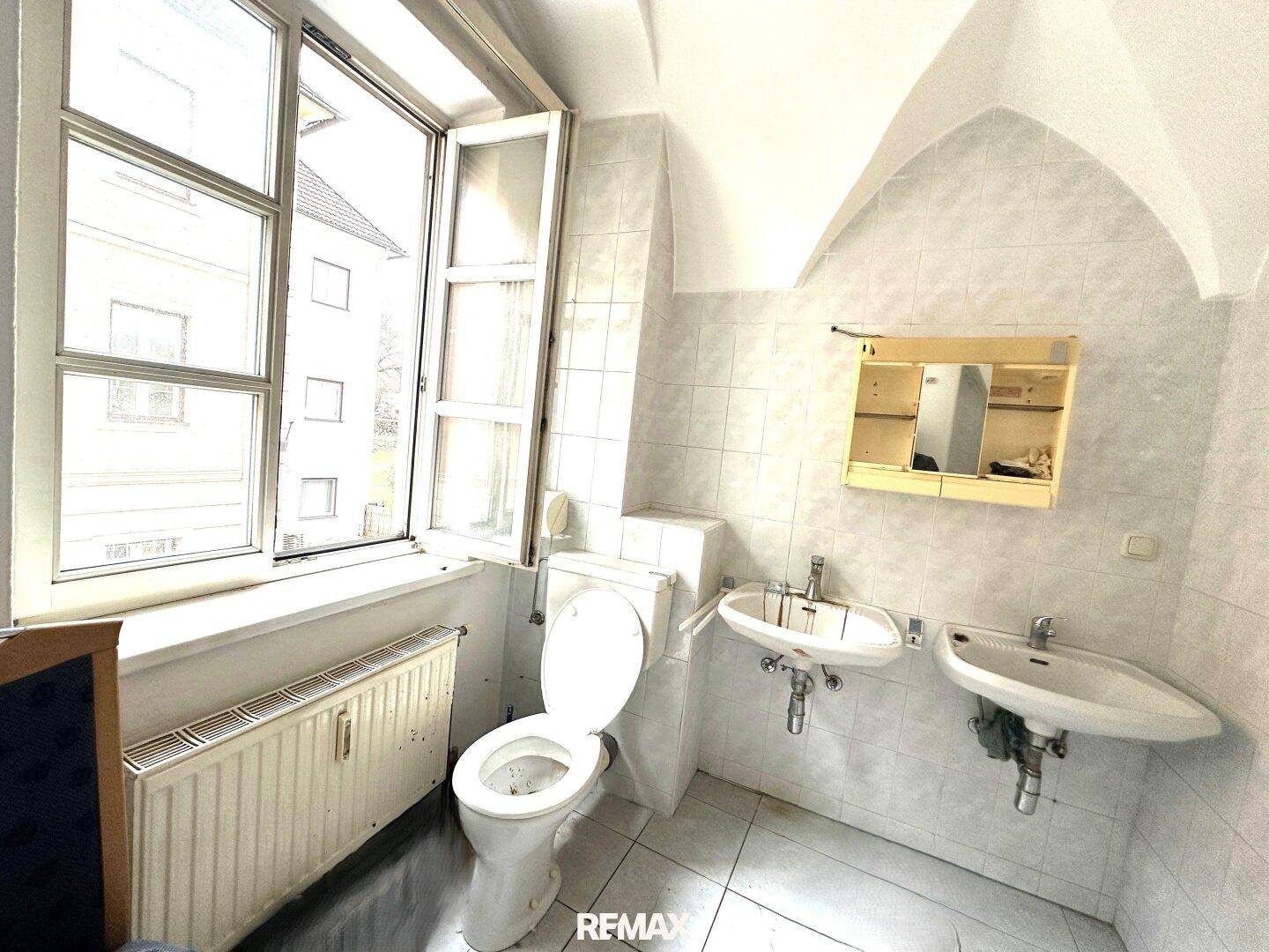 Helles Badezimmer mit zwei Waschbecken, Toilette und Fenster unter einer gewölbten Decke.
