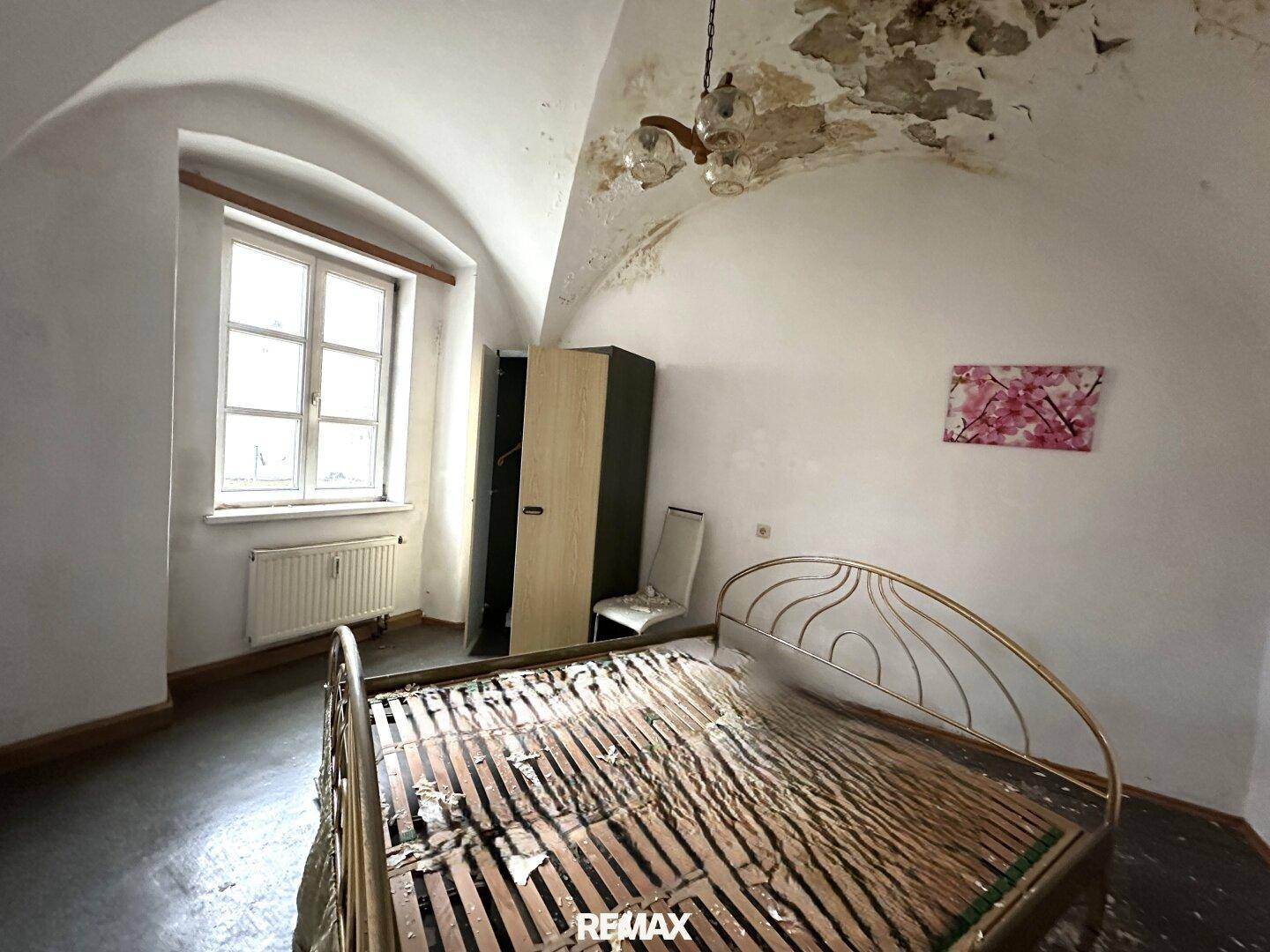Schlafzimmer mit gewölbter Decke, Fenster und einem Bettgestell, das Renovierung benötigt.