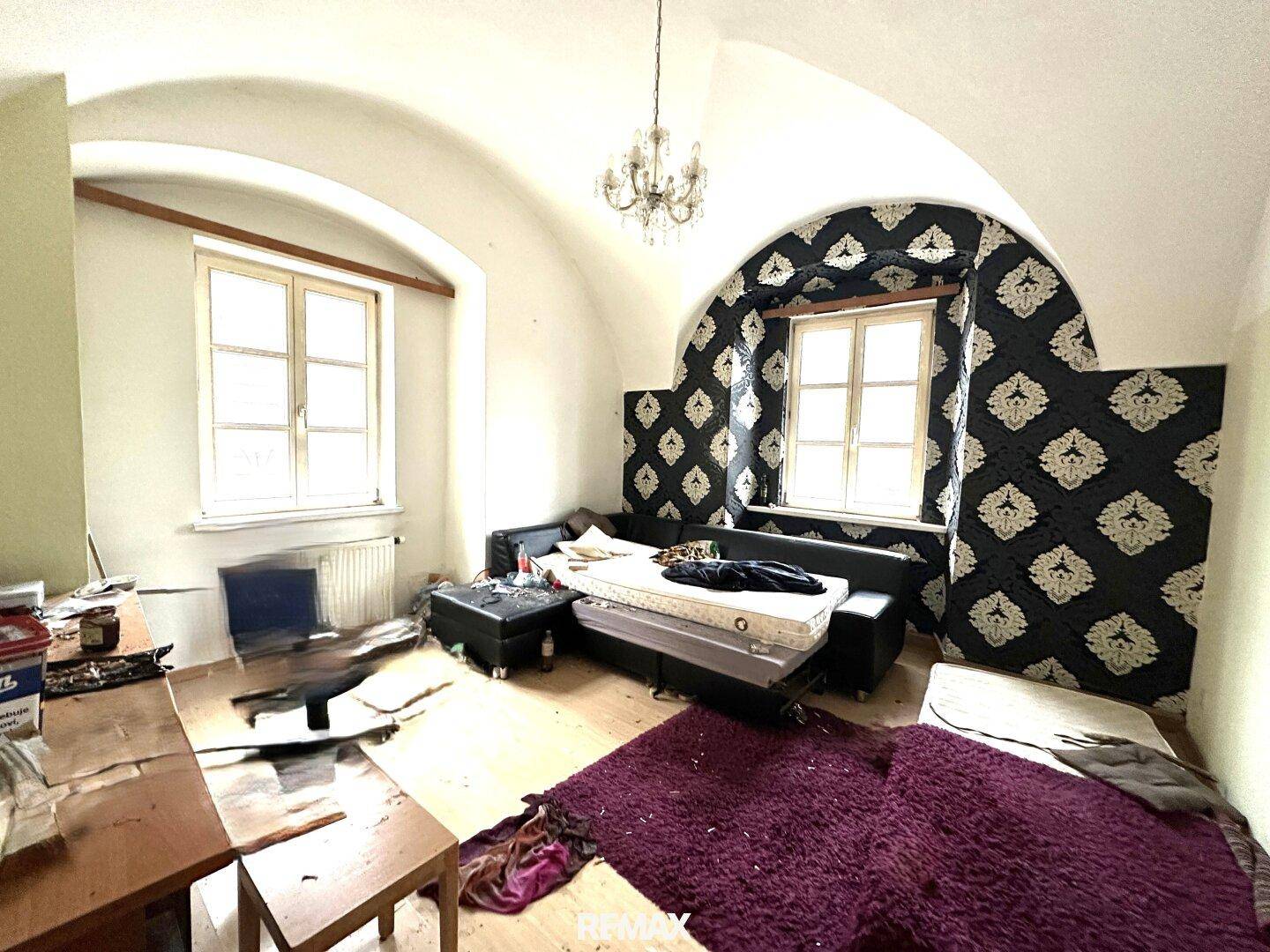 Geräumiges Wohnzimmer mit gewölbter Decke, Holzboden und dekorativer Tapete.