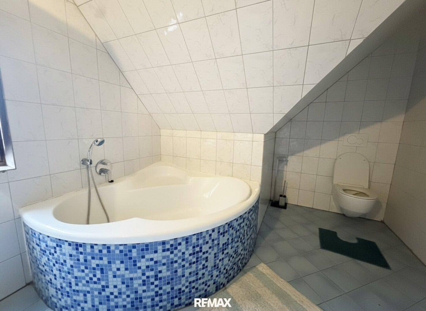 Badezimmer im Dachgeschoss mit Eckbadewanne, WC und blauen Mosaikfliesen.