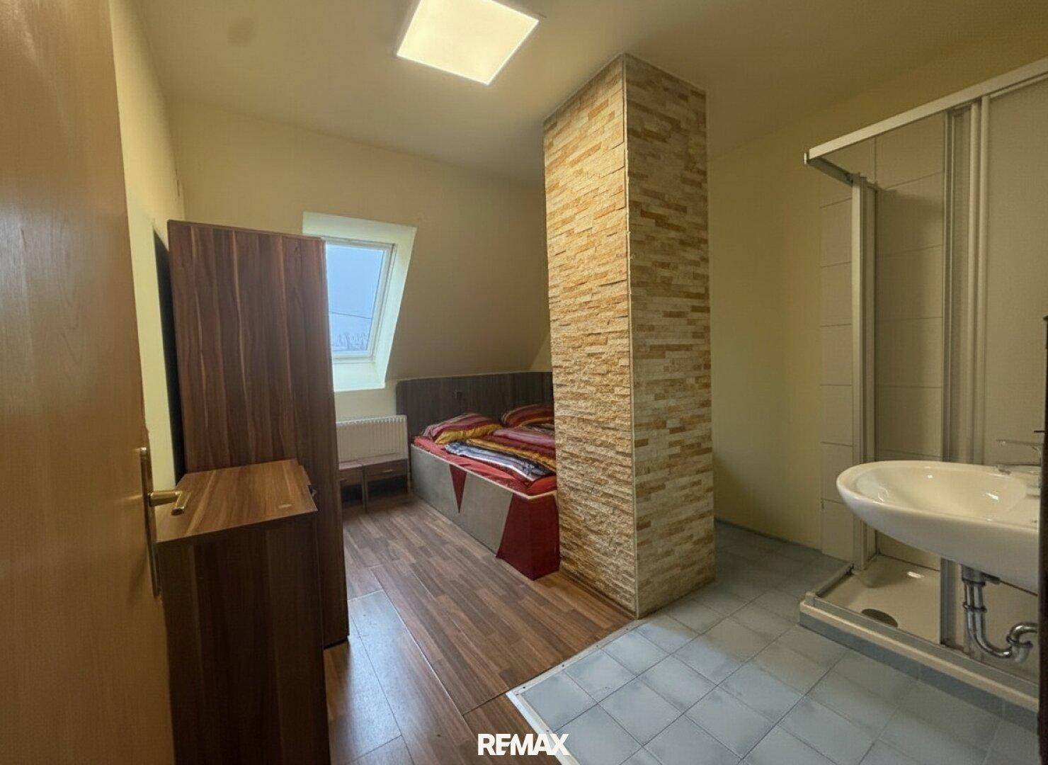 Schlafzimmer im Dachgeschoss mit Holzboden, Dusche und Waschbecken.