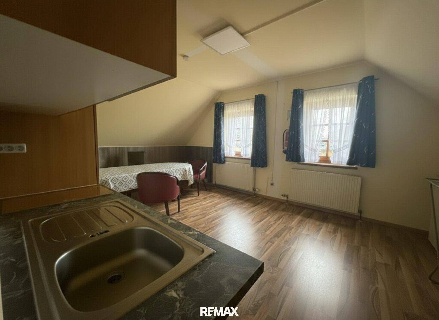 Dachgeschosszimmer mit kleiner Küchenzeile, Essbereich und Holzboden.