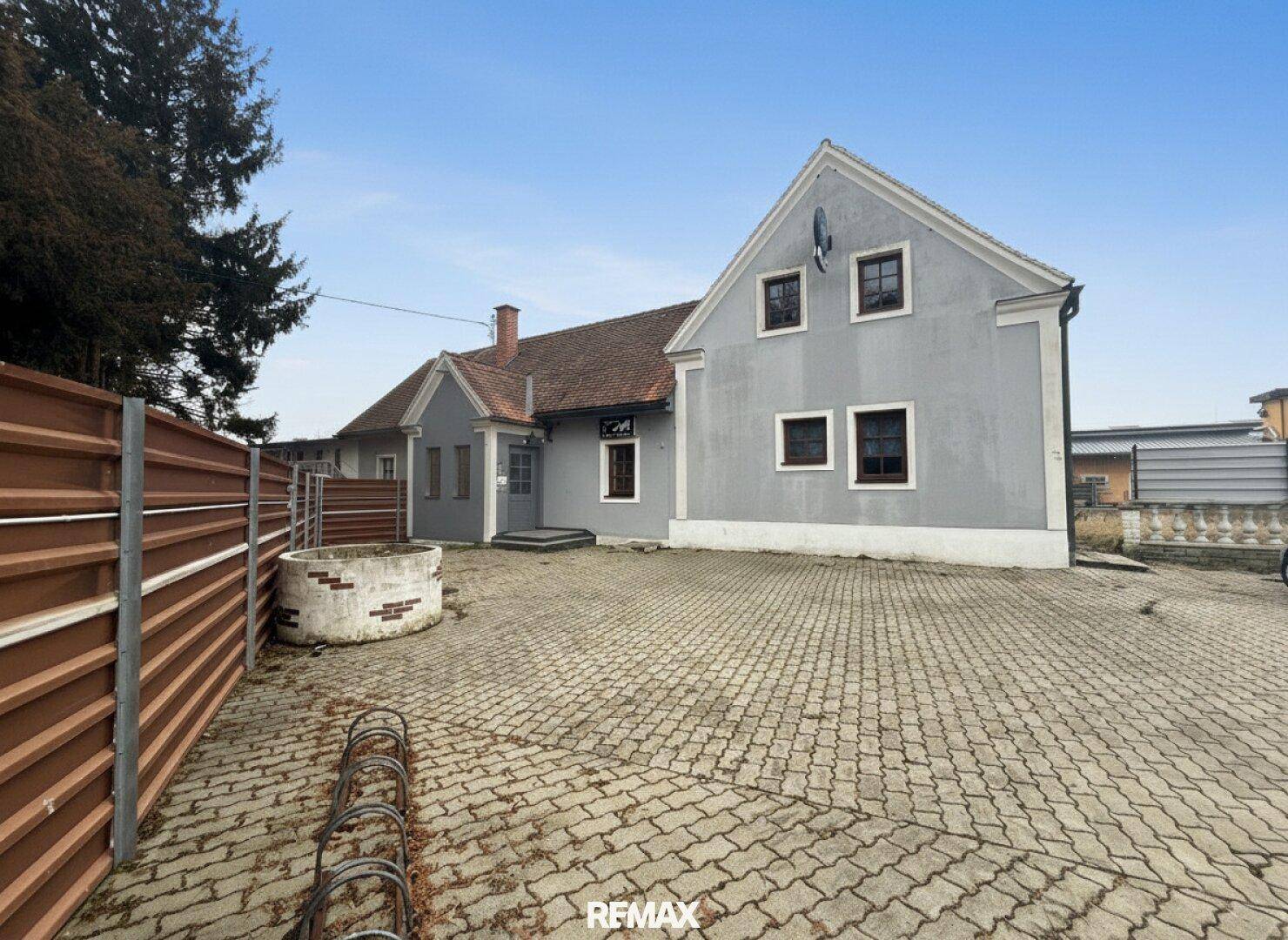 Graues Wohnhaus mit gepflastertem Vorplatz und traditioneller Architektur.