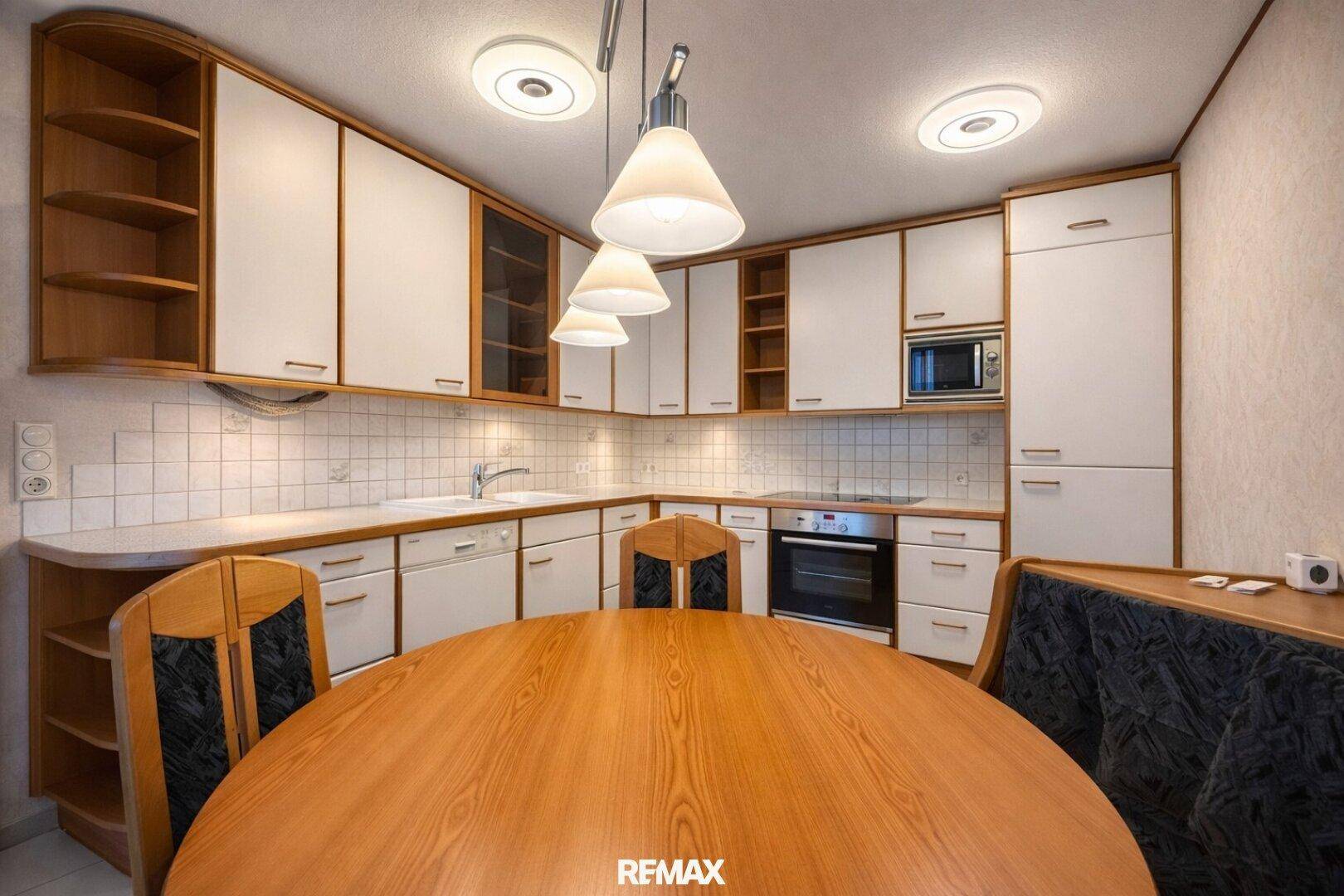 Helle Einbauküche mit weißen Schränken, Holzelementen und integriertem Essbereich.