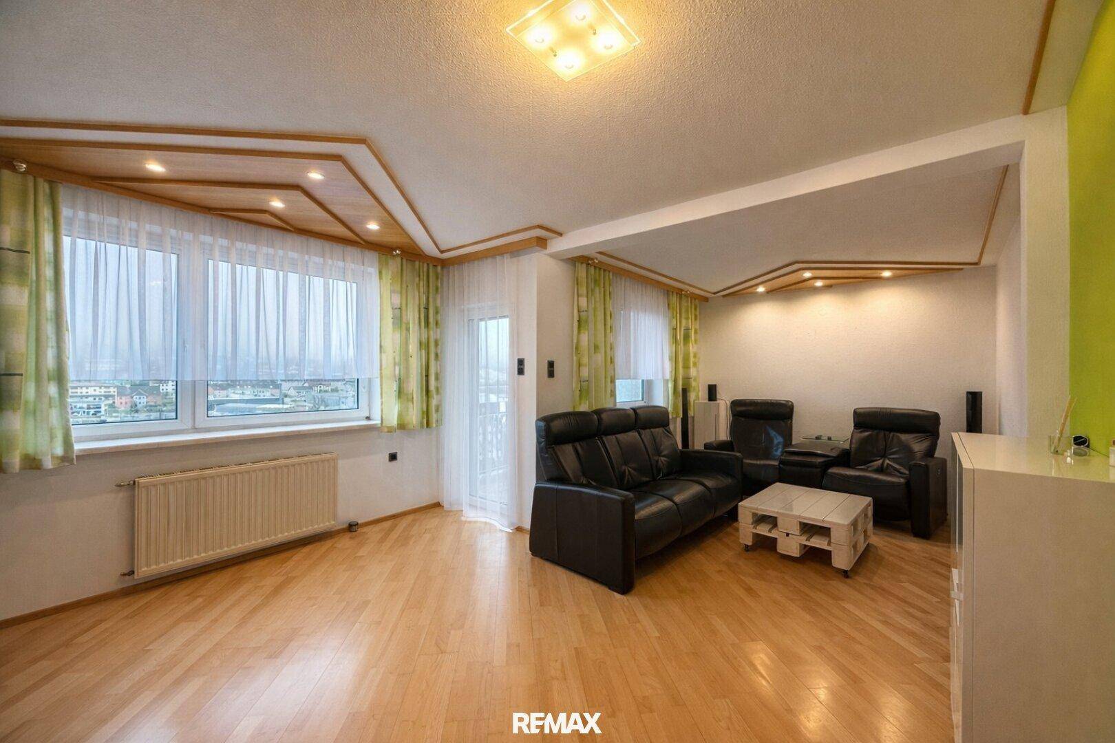 Helles Wohnzimmer mit Holzboden, großen Fenstern und Blick auf die Umgebung.