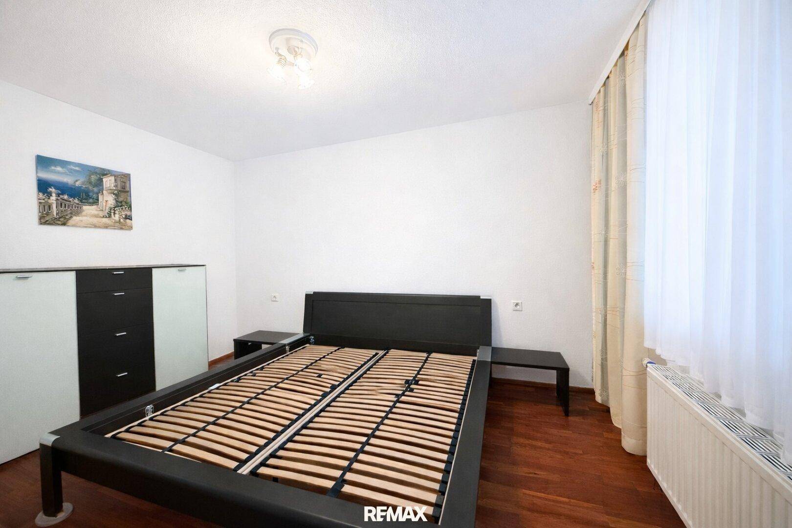 Modernes Schlafzimmer mit dunklem Bettrahmen und hellem Holzboden.