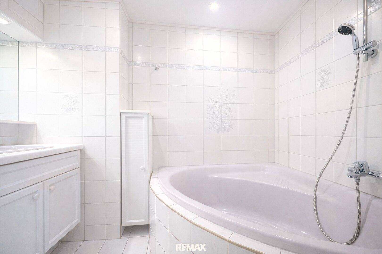Weiß gefliestes Badezimmer mit Eckbadewanne und integrierter Dusche.