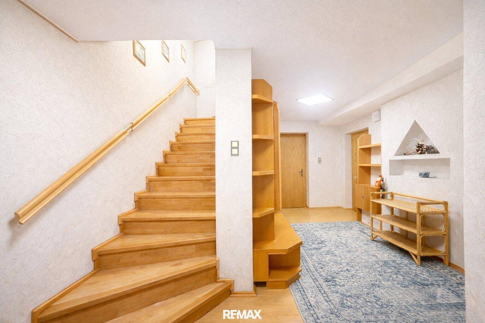 Heller Flur mit Holztreppe und Teppichboden, der zu den oberen Etagen führt.