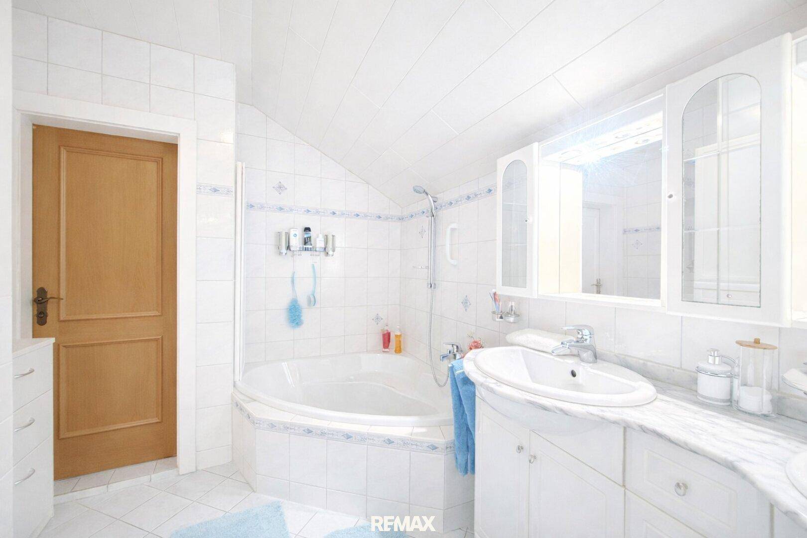 Weiß gefliestes Badezimmer mit Badewanne, Waschtisch und Spiegelschrank.