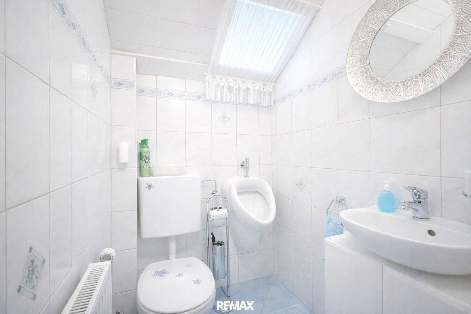 Separates WC mit Urinal, Dachfenster und weißen Fliesen.