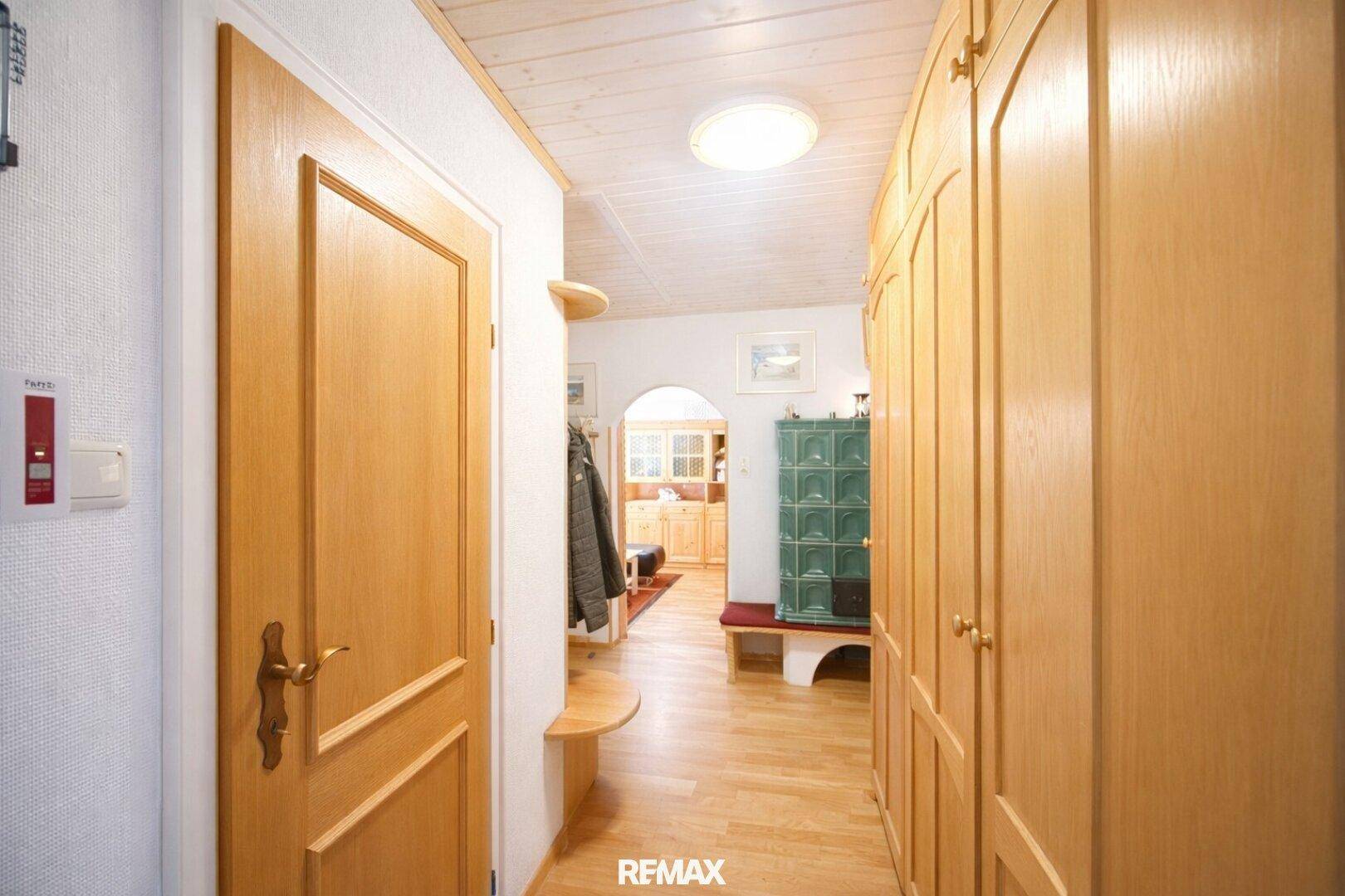 Heller Flur mit Holzdielenboden, Einbauschränken und einem traditionellen Kachelofen.