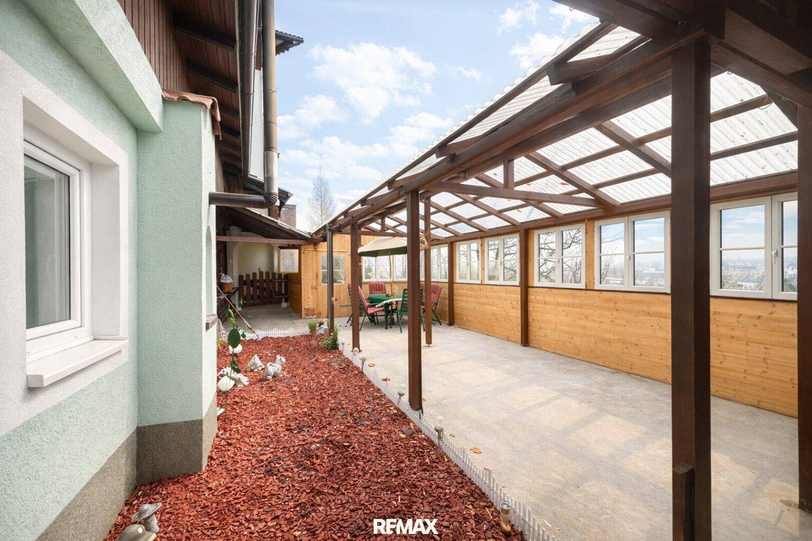 Überdachter Außenbereich mit Holzkonstruktion und Fenstern, ideal als Wintergarten oder Terrasse.