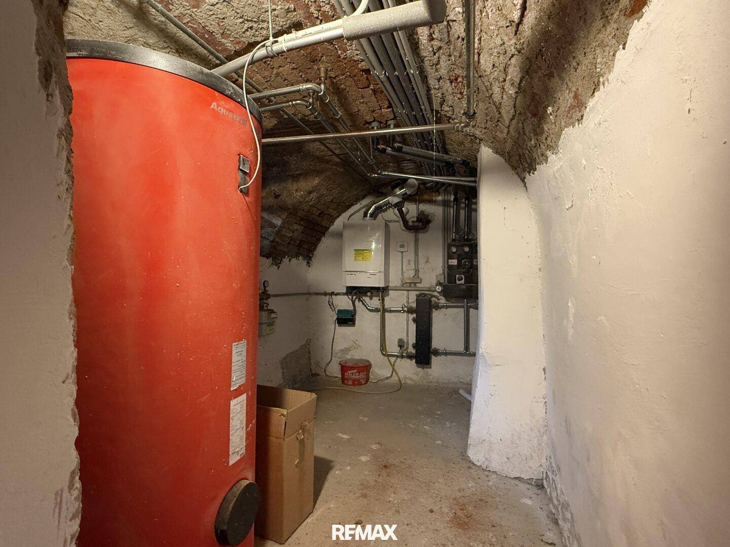 Gewölbekeller mit großem roten Warmwasserspeicher und sichtbaren Rohrleitungen.