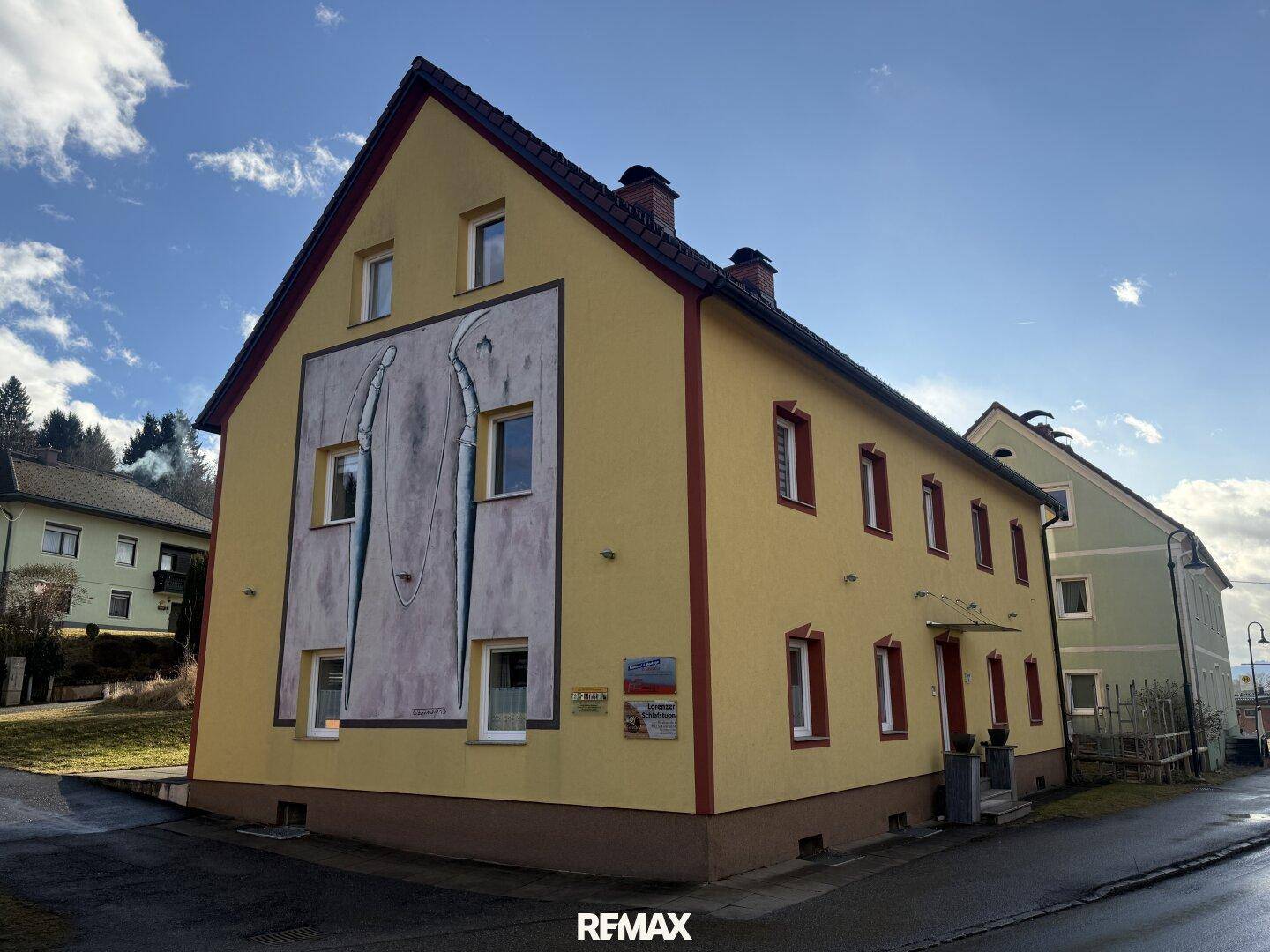 Gelbes Gebäude mit markanter Fassadenmalerei und roten Akzenten unter blauem Himmel.