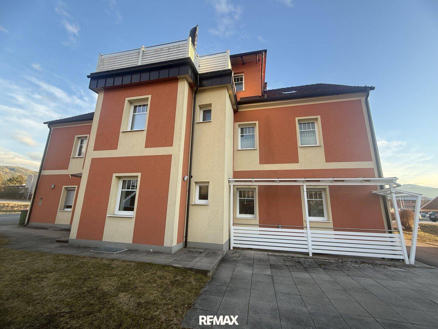 Rückansicht des Gebäudes mit oranger Fassade, einem kleinen Balkon und überdachtem Bereich.