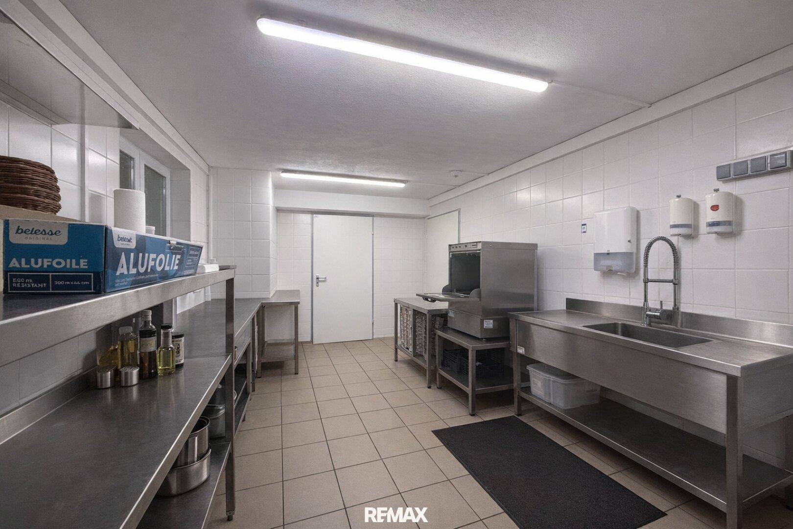 Professionelle Großküche mit Edelstahlarbeitsflächen, Spülbecken und industrieller Spülmaschine, bereit für den Betrieb.