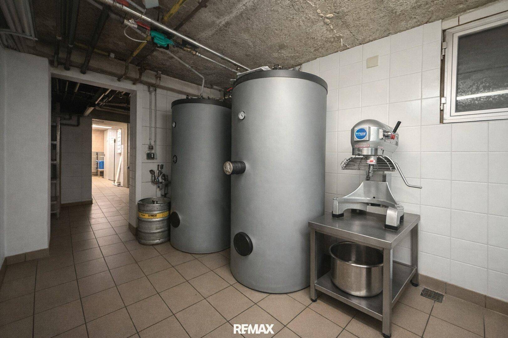 Technikraum mit großen Warmwasserspeichern und einer professionellen Küchenmaschine, geflieste Wände.