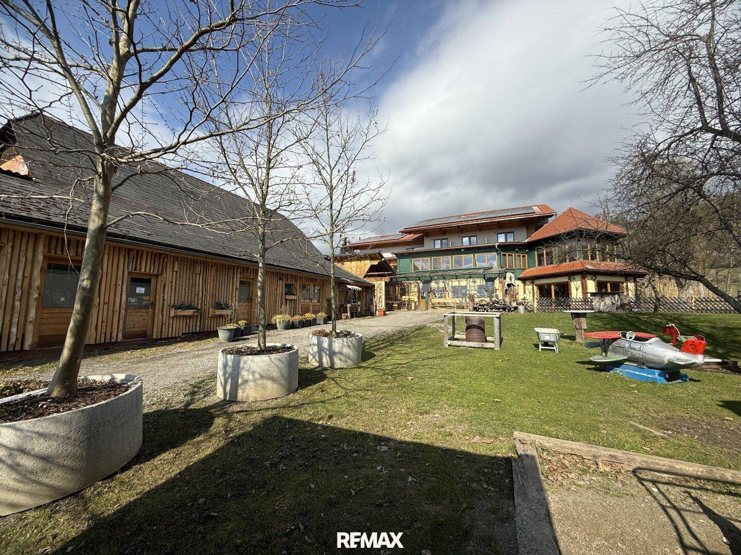 Gebäudekomplex mit Holzhäusern und einem großen Gartenbereich mit Spielgeräten und Bäumen.