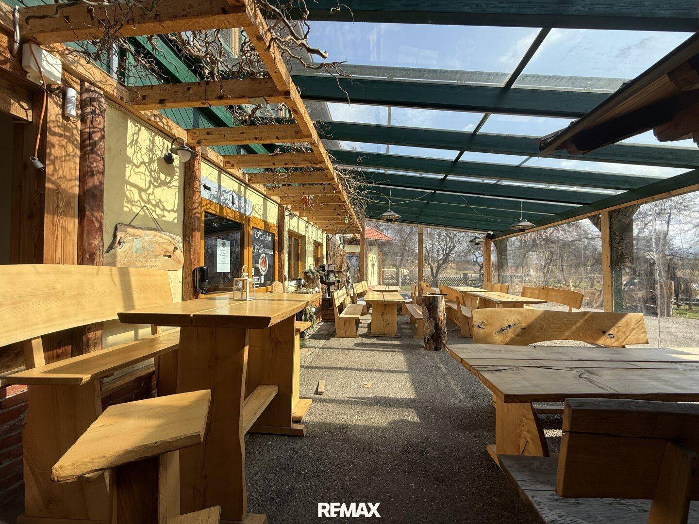 Überdachte Außenterrasse mit Holztischen und Bänken, ideal für Mahlzeiten im Freien.