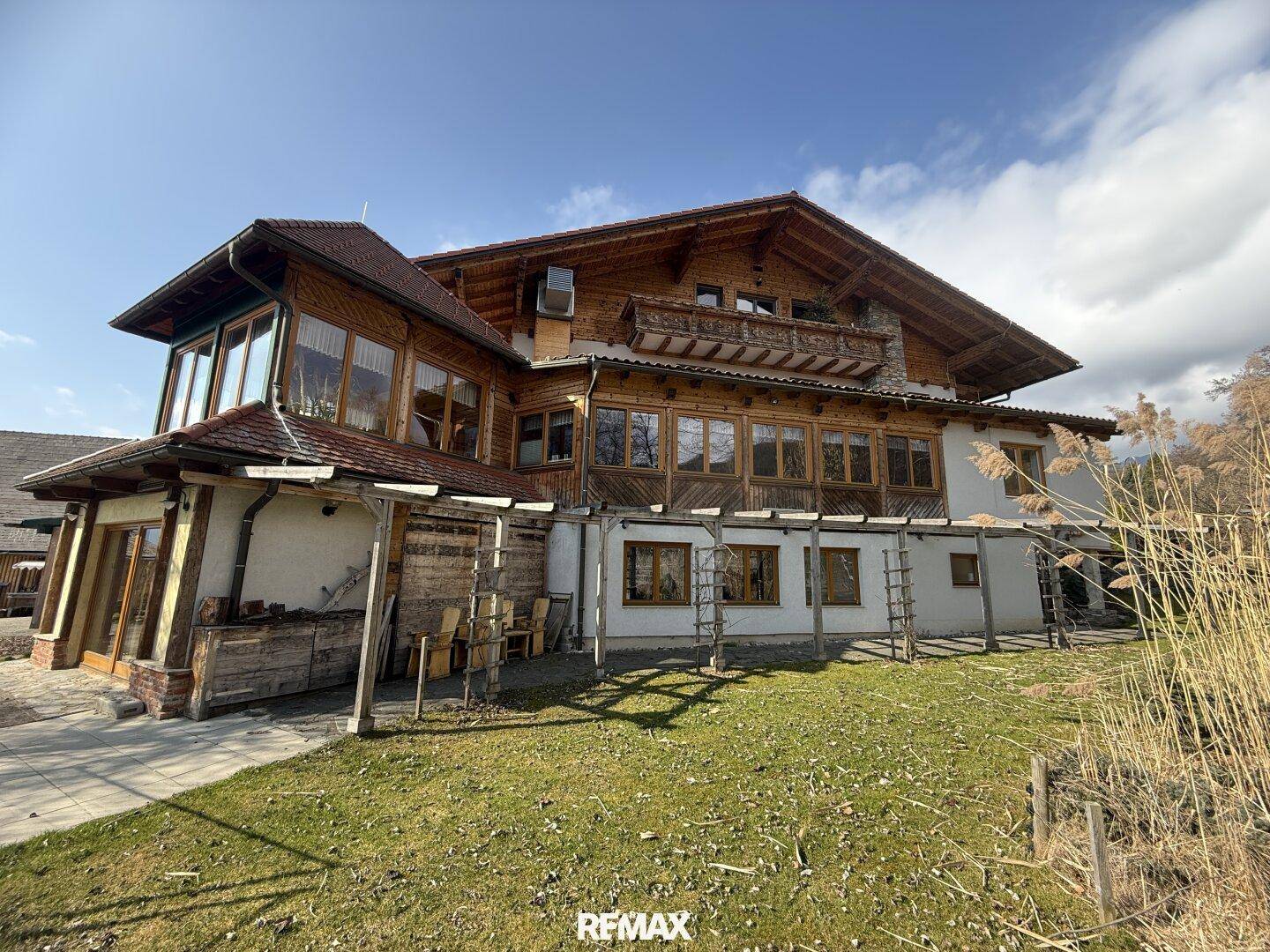 Großes Holzhaus mit mehreren Fenstern und einem Balkon, umgeben von einer Wiese und Schilf.