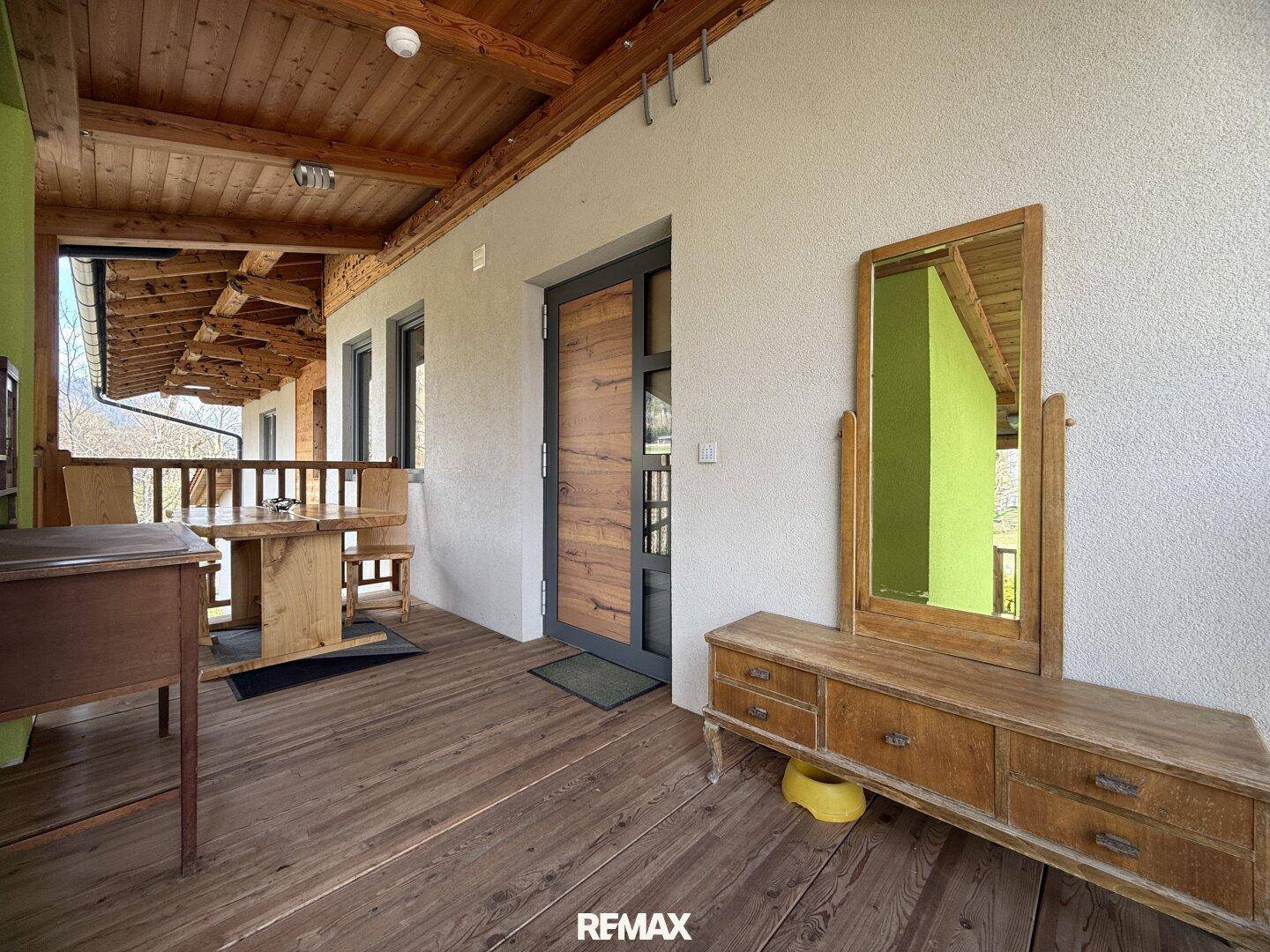Eingangsbereich mit Holzboden, einer Holzkommode mit Spiegel und einem Tisch auf einer überdachten Terrasse.