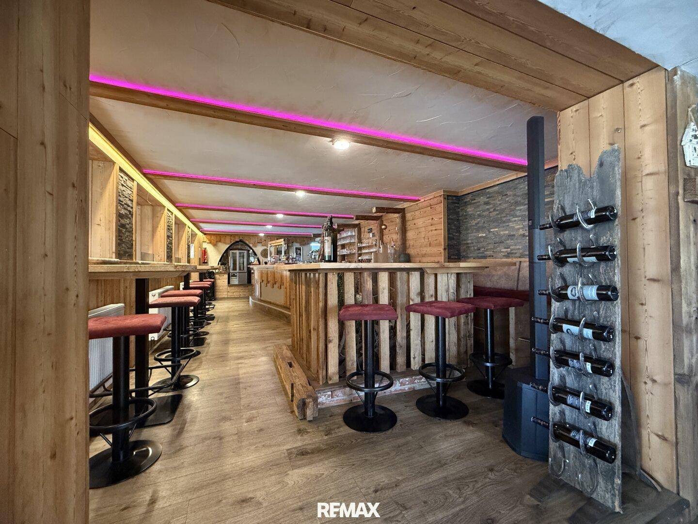 Barbereich mit rustikaler Holzeinrichtung, modernen pinken LED-Akzenten und einem dekorativen Weinregal.