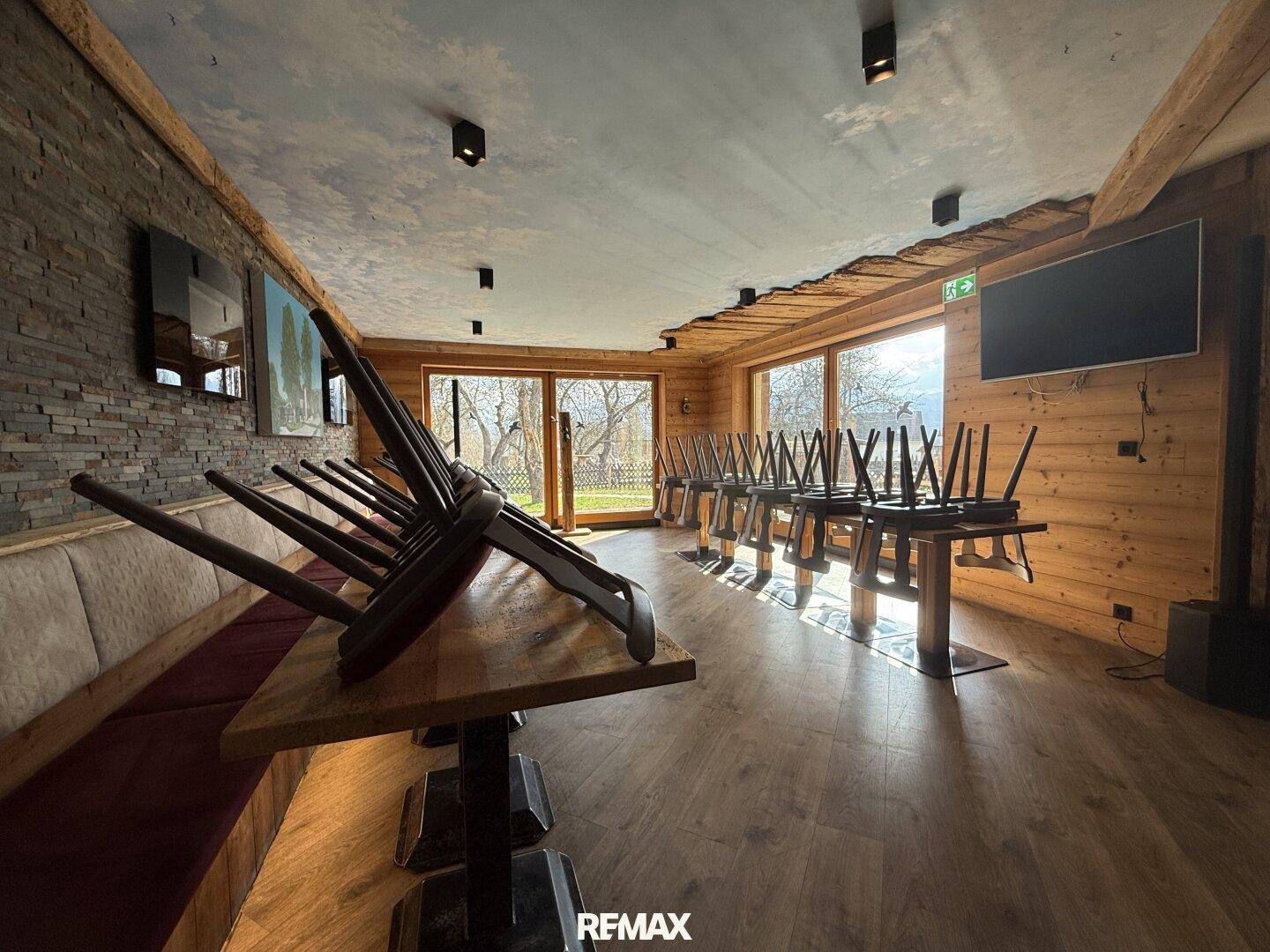 Geräumiger Speisesaal mit Holzboden, Steinwandakzenten und Tischen mit umgedrehten Stühlen.