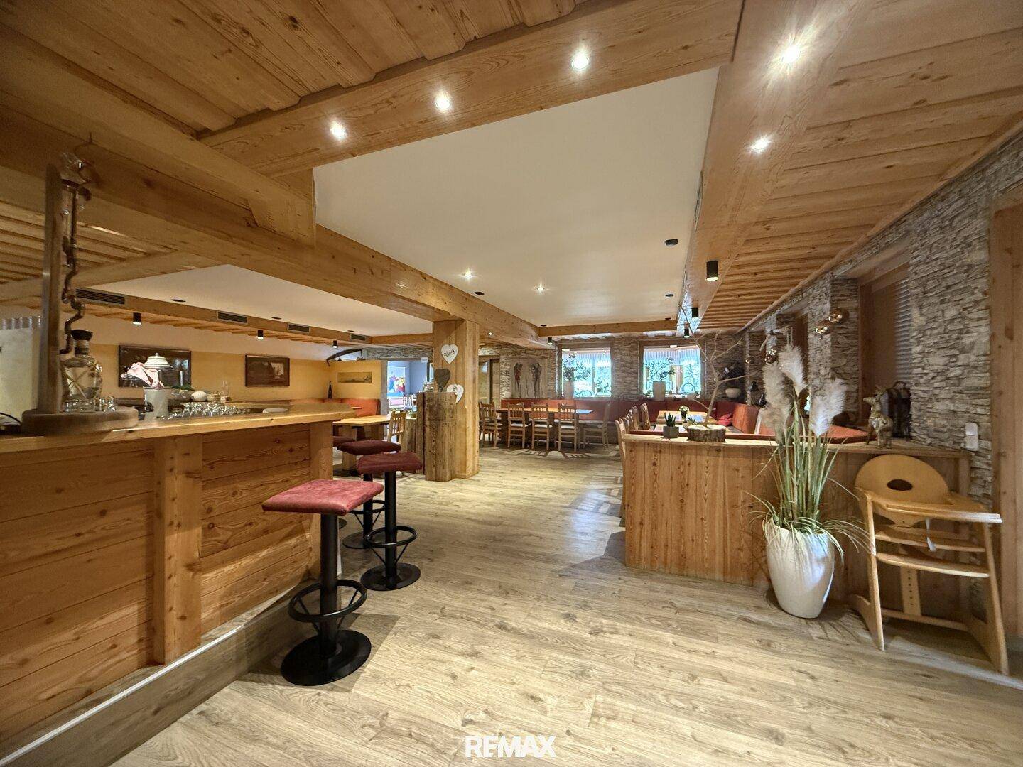 Geräumiger Speisesaal mit Holzboden, Holzbalken und einer Bar, dekoriert mit Pflanzen.