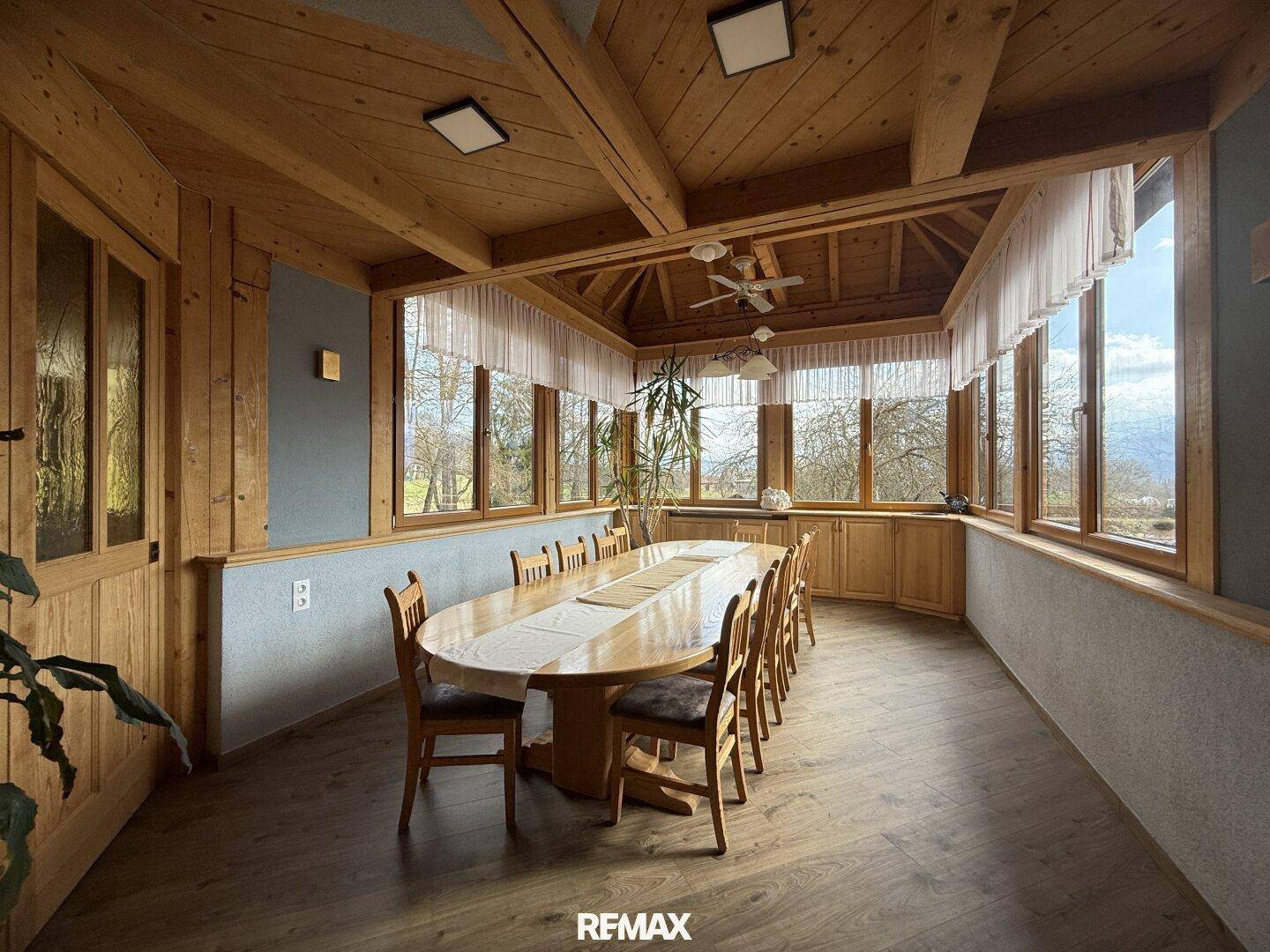 Heller Speisesaal mit vielen Fenstern, Holzboden und einem großen ovalen Esstisch.