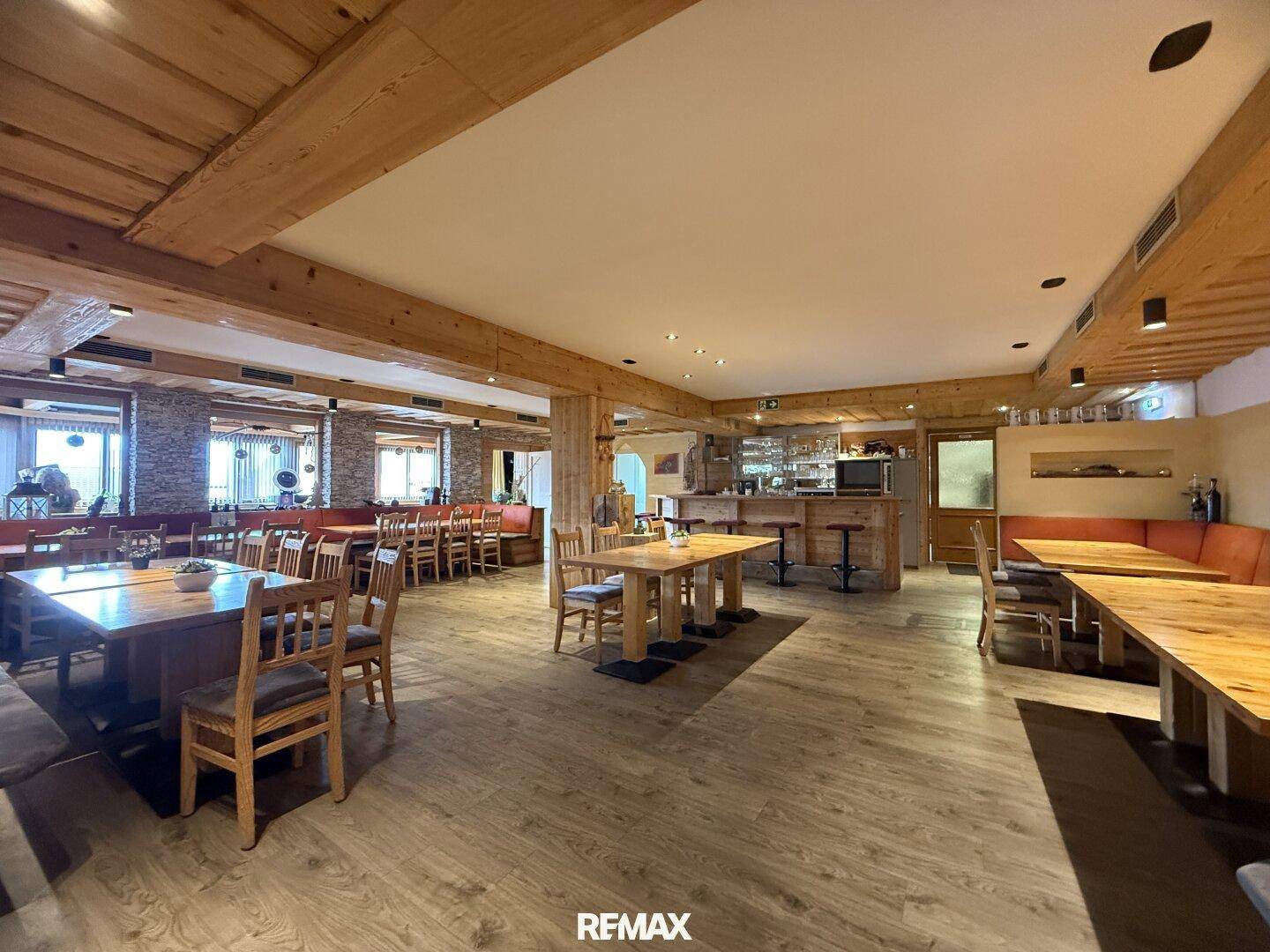 Gemütlicher Speisesaal mit rustikalen Holztischen und Bänken, im Hintergrund ein Barbereich.