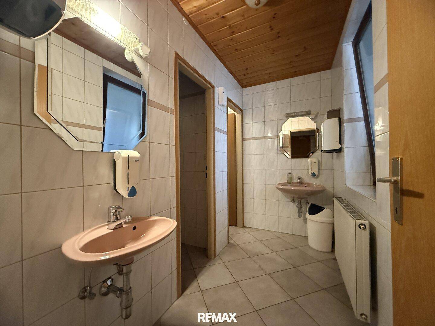 Geräumige öffentliche Toilette mit mehreren Waschbecken und Spiegeln, hell geflieste Wände.