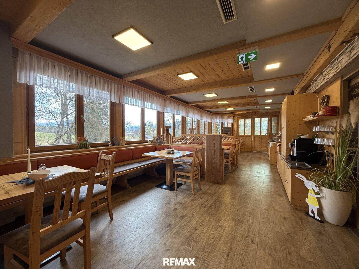 Heller Speisesaal mit Holzboden, Holzbalken und großen Fenstern, die viel Tageslicht hereinlassen.