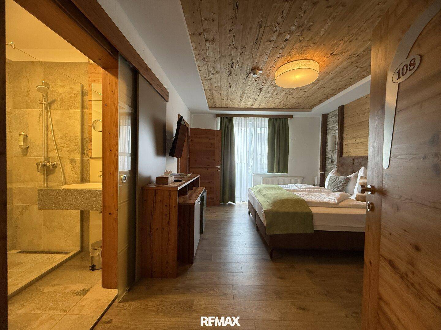 Gemütliches Schlafzimmer mit Holzboden, Holzwänden und einem Doppelbett, mit Zugang zum Badezimmer.