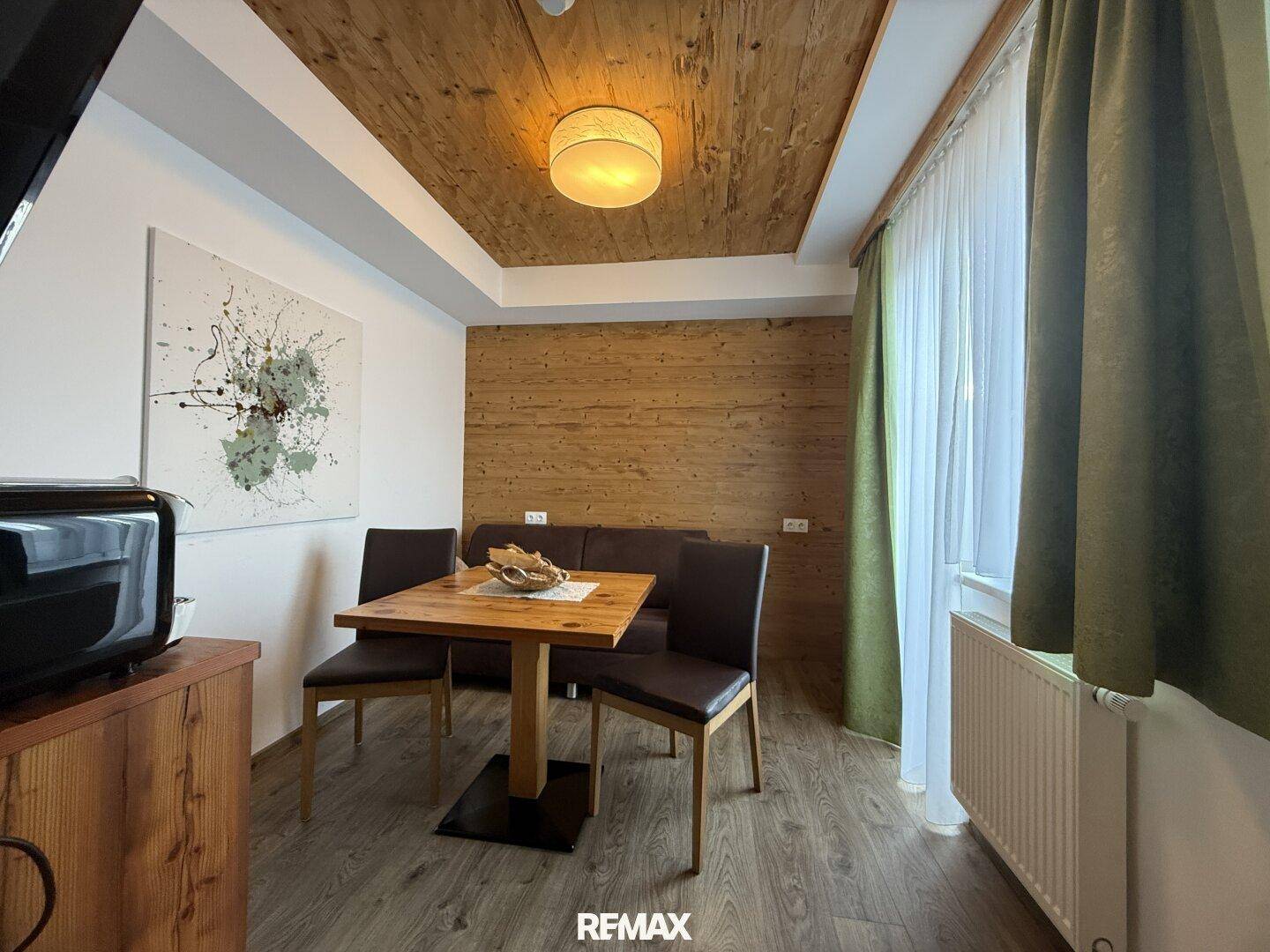 Gemütlicher Essbereich mit Holztisch, bequemen Stühlen und einer Holzvertäfelung an Decke und Wand.