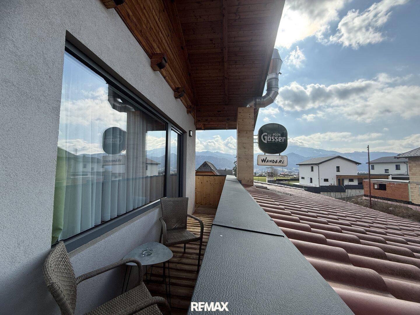 Balkon mit Sitzgelegenheiten, Blick über ein Ziegeldach auf die umliegende Berglandschaft.