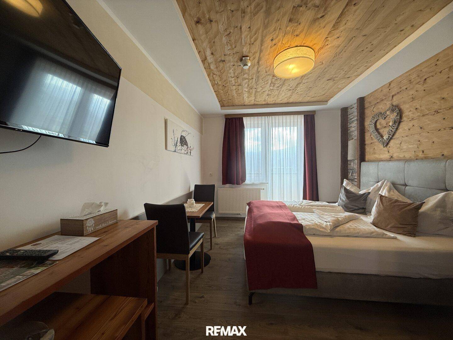 Gemütliches Schlafzimmer mit Holzbalkendecke, Doppelbett und einem kleinen Essbereich.