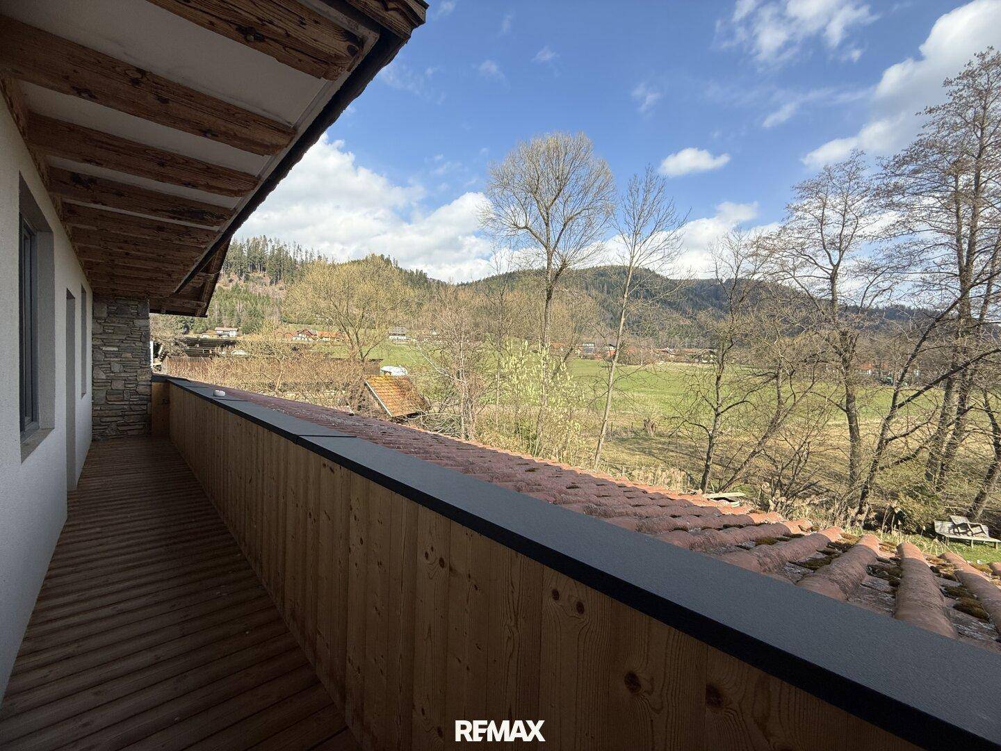 Langer Balkon mit Holzverkleidung und weitem Blick auf grüne Hügel und bewaldete Landschaft.