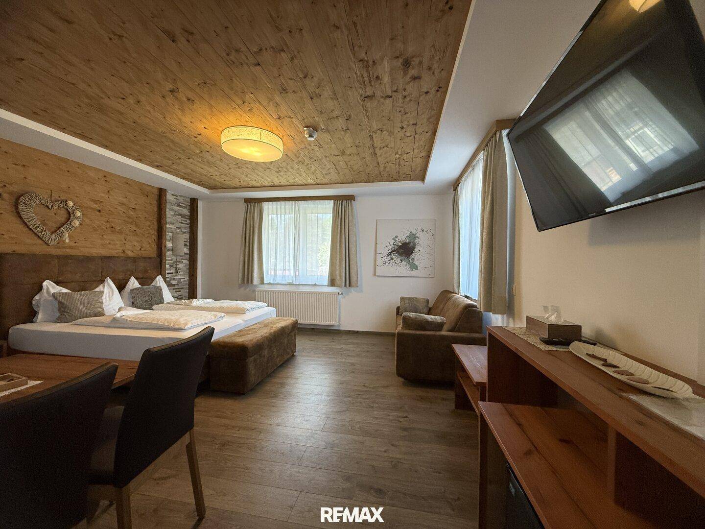 Geräumiges Schlafzimmer mit Holzbalkendecke, großem Bett, Sofa und Flachbildfernseher.