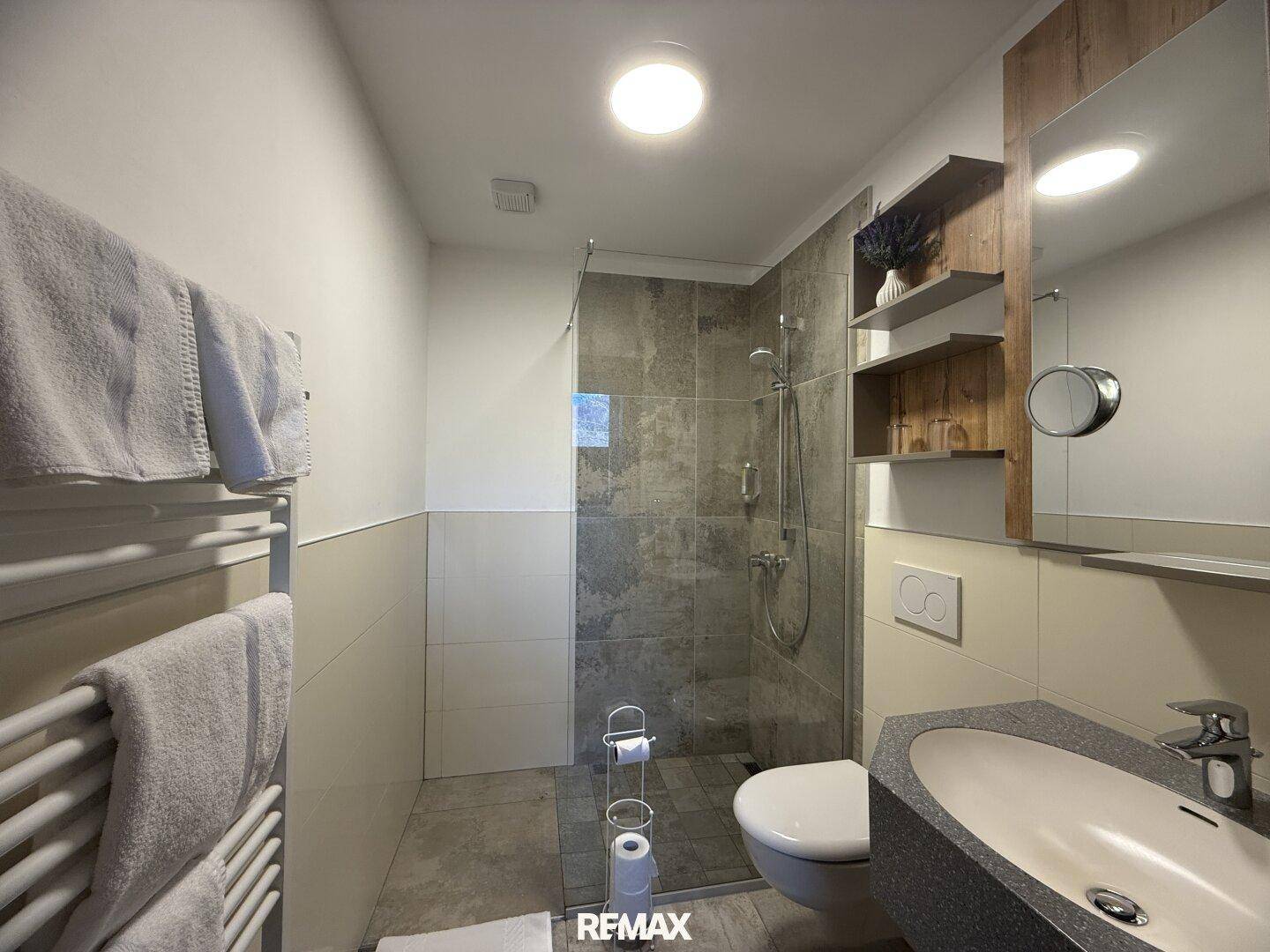 Modernes Badezimmer mit begehbarer Dusche, Hänge-WC und Waschtisch, hell gefliest.