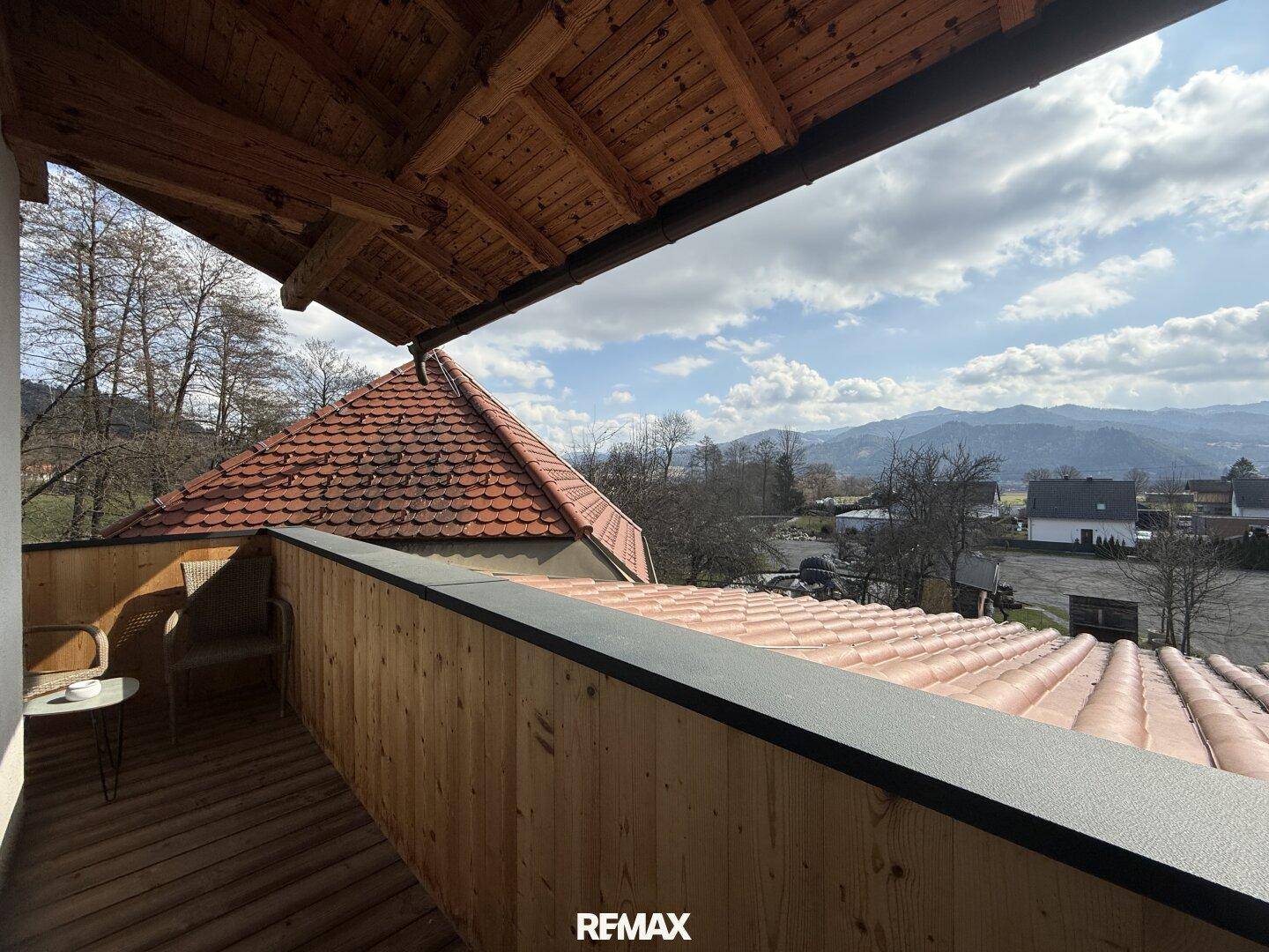 Balkon mit Sitzgelegenheiten, bietet einen Ausblick über ein Ziegeldach auf die umliegende Bergwelt.