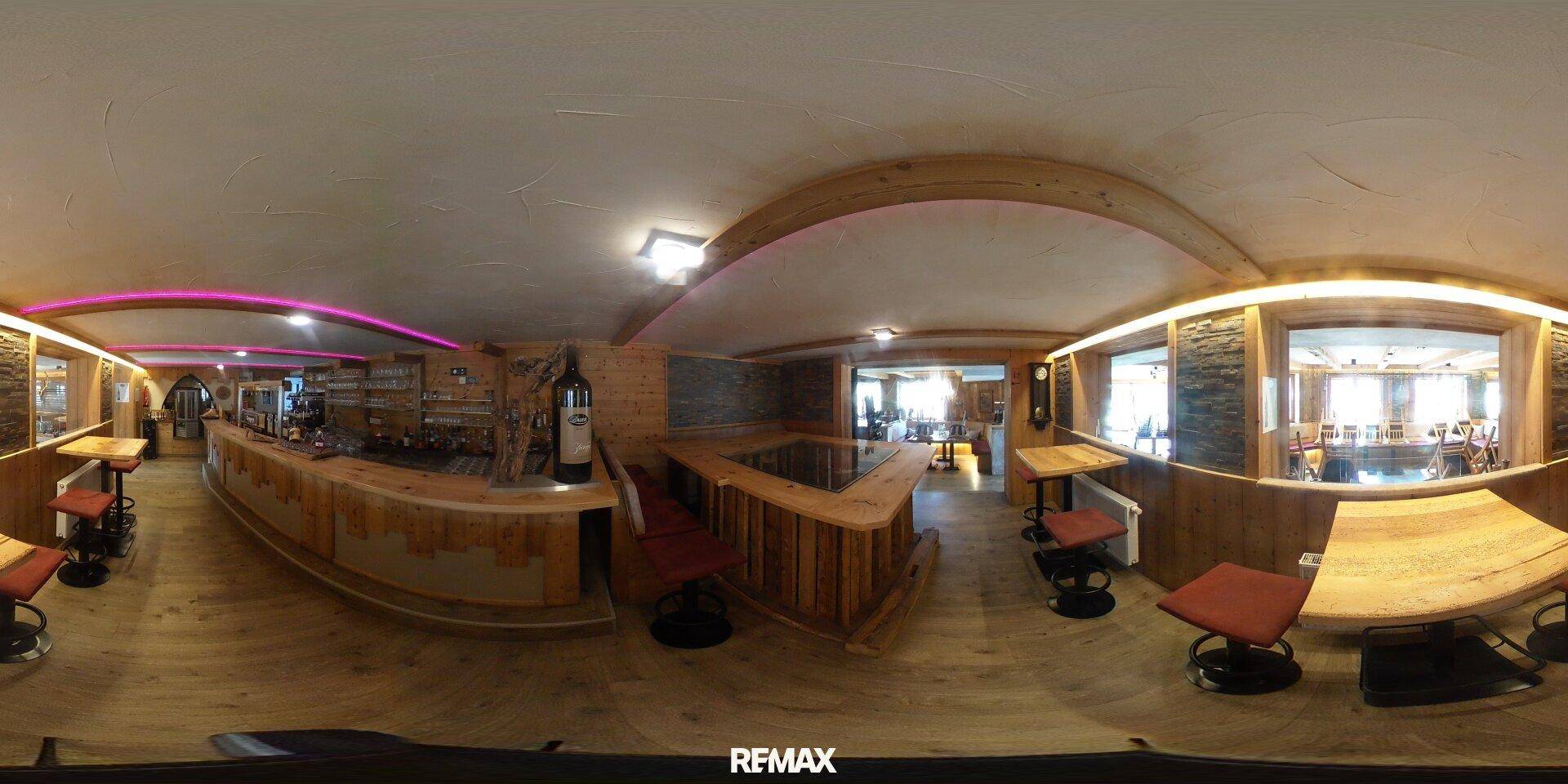 Panoramablick auf einen rustikalen Barbereich mit Holzelementen, Hockern und indirekter Beleuchtung.