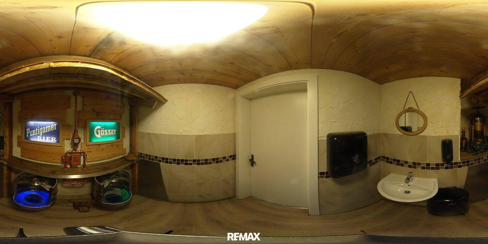 Panoramablick in eine öffentliche Toilette mit Urinalen, Waschbecken und einer weißen Tür.