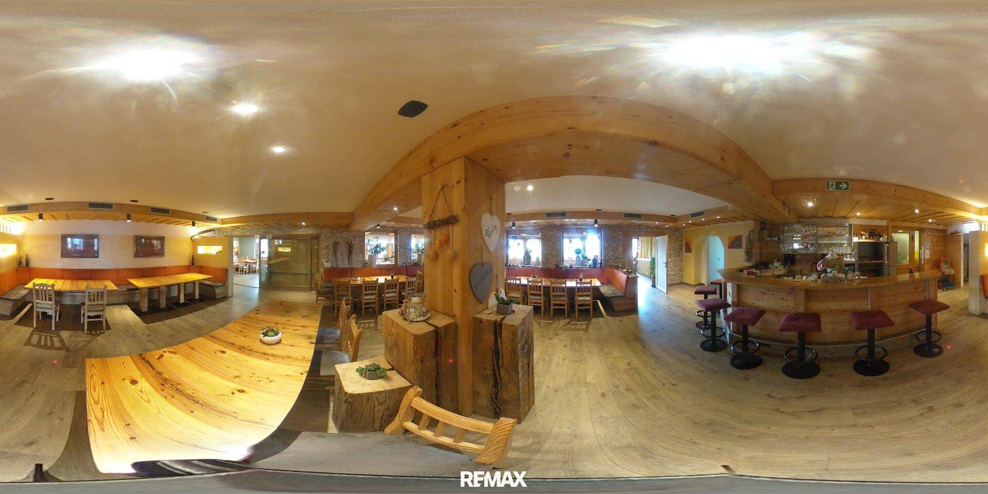 Panoramablick in ein großes Restaurant mit Bar, zahlreichen Tischen und rustikaler Holzdekoration.