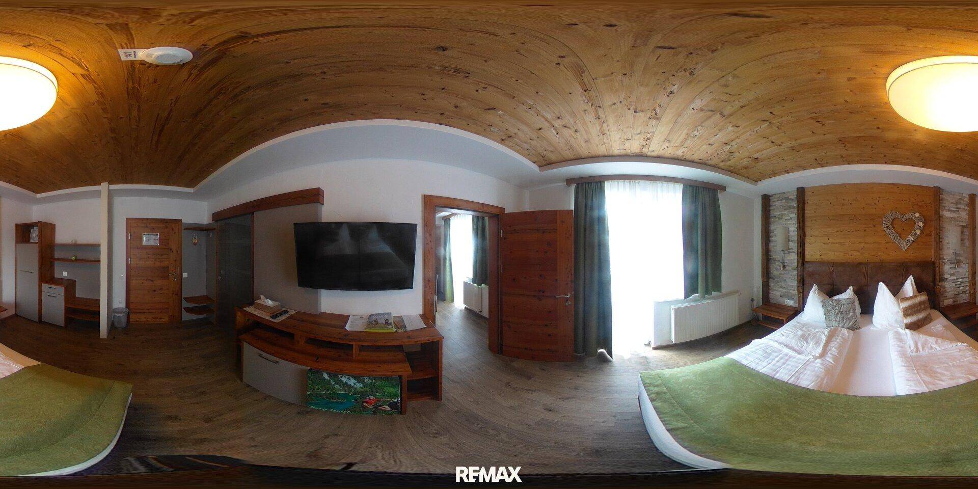 Schlafzimmer mit zwei Betten, Flachbildfernseher und einer warmen Holzbalkendecke.