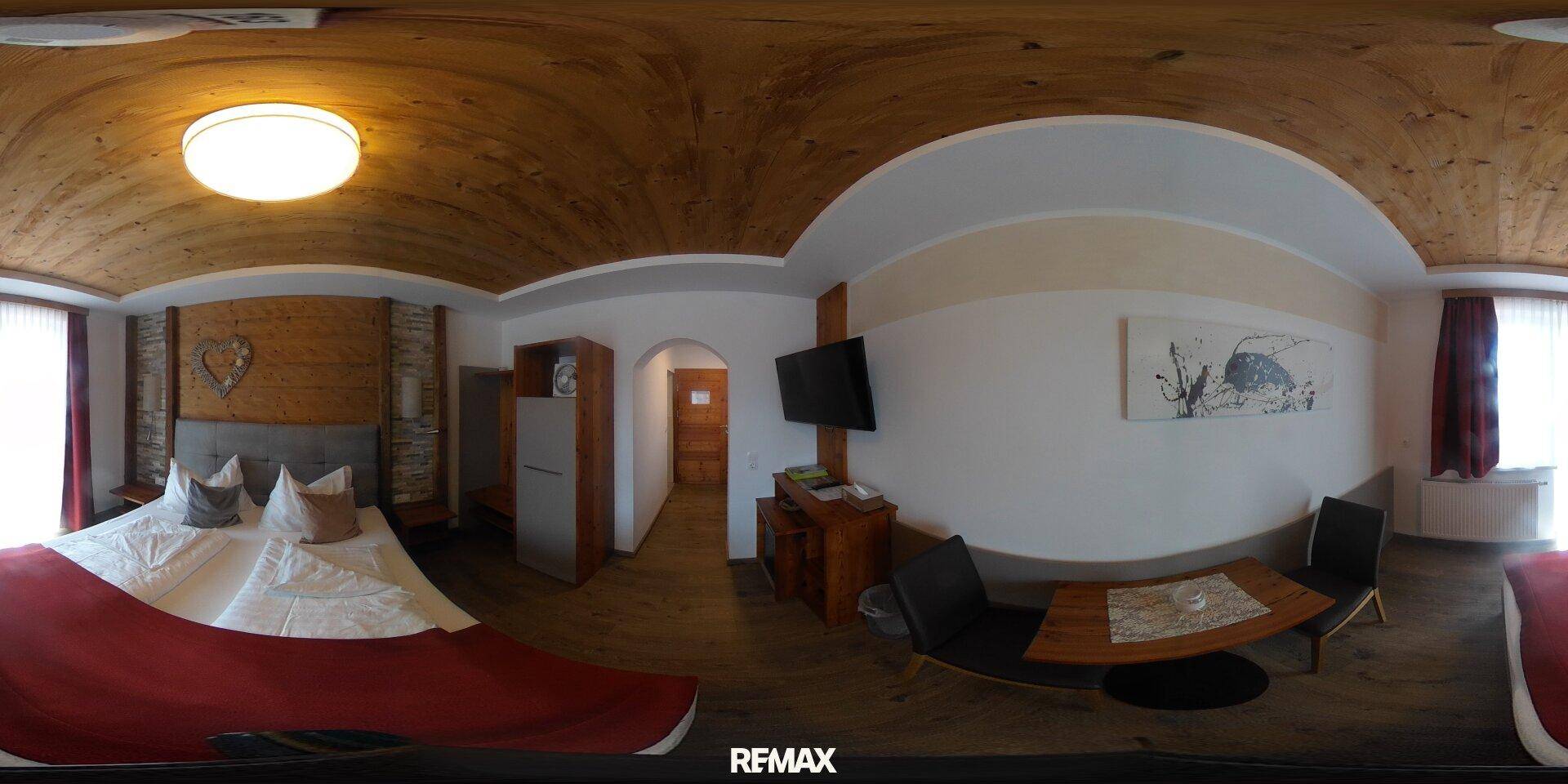 Gemütliches Schlafzimmer mit Doppelbett, kleinem Essbereich und Holzbalkendecke.