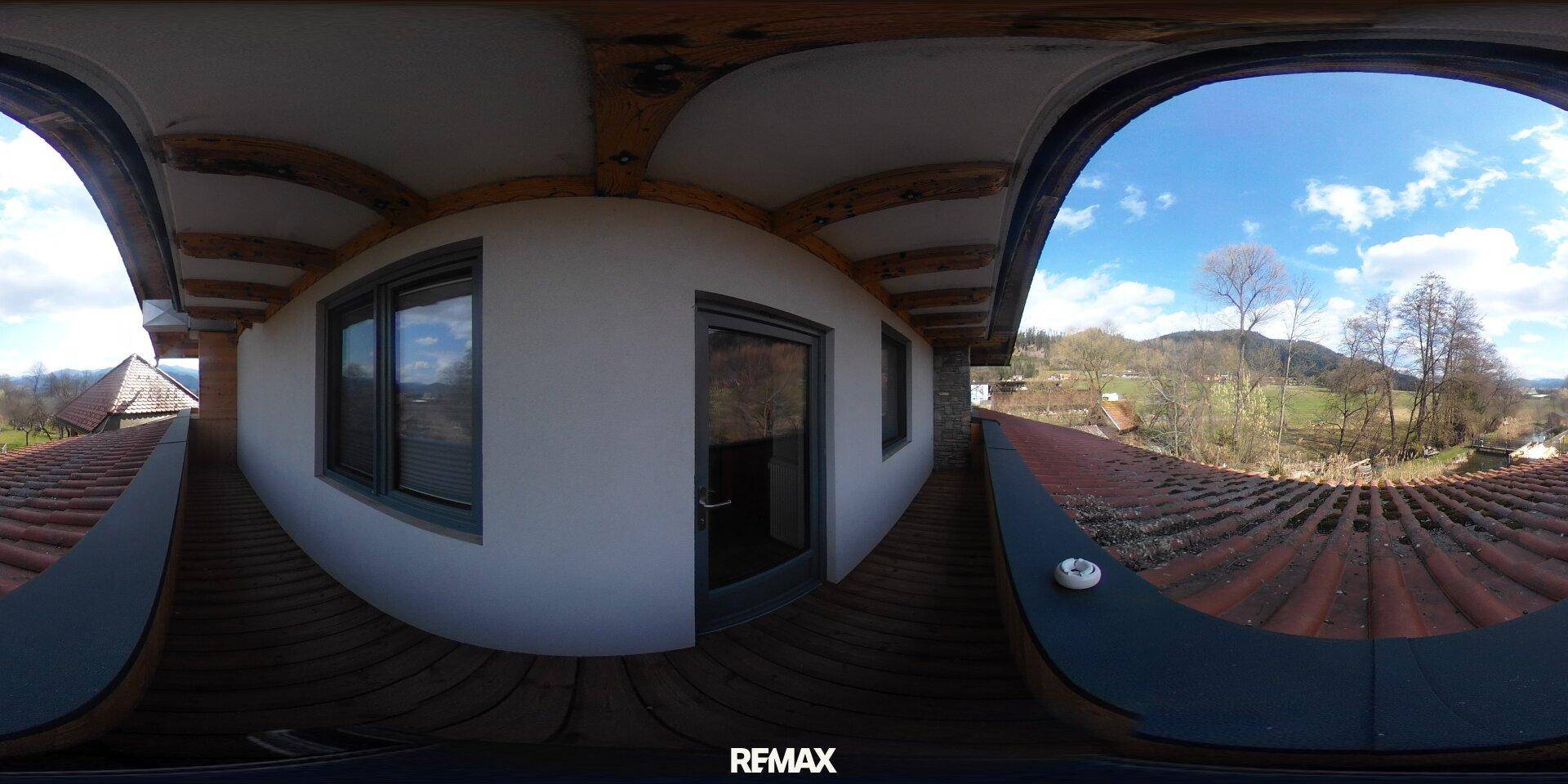 Panoramablick vom Balkon auf die Gebäudefassade, Ziegeldächer und die grüne Landschaft.